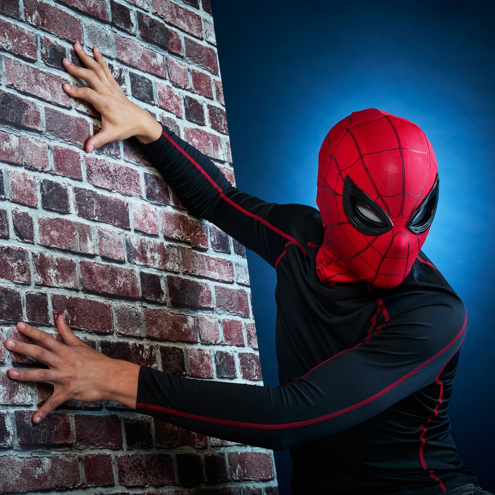 Person wearing the Spider-Man mask beside a brick wall