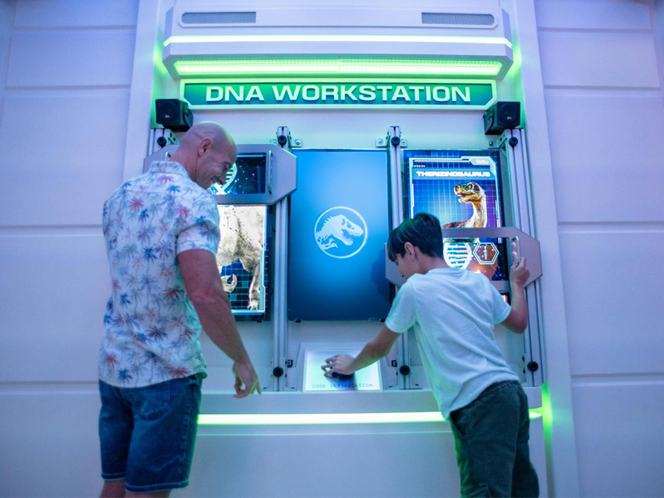 A father and son interact with the DNA Workstation inside Jurassic World: Escape