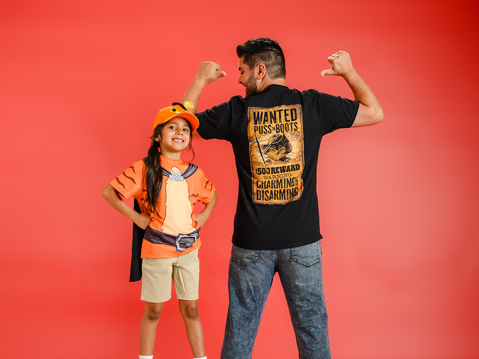A child wearing Puss in Boots character headwear and clothing beside an adult in a Puss in Boots shirt