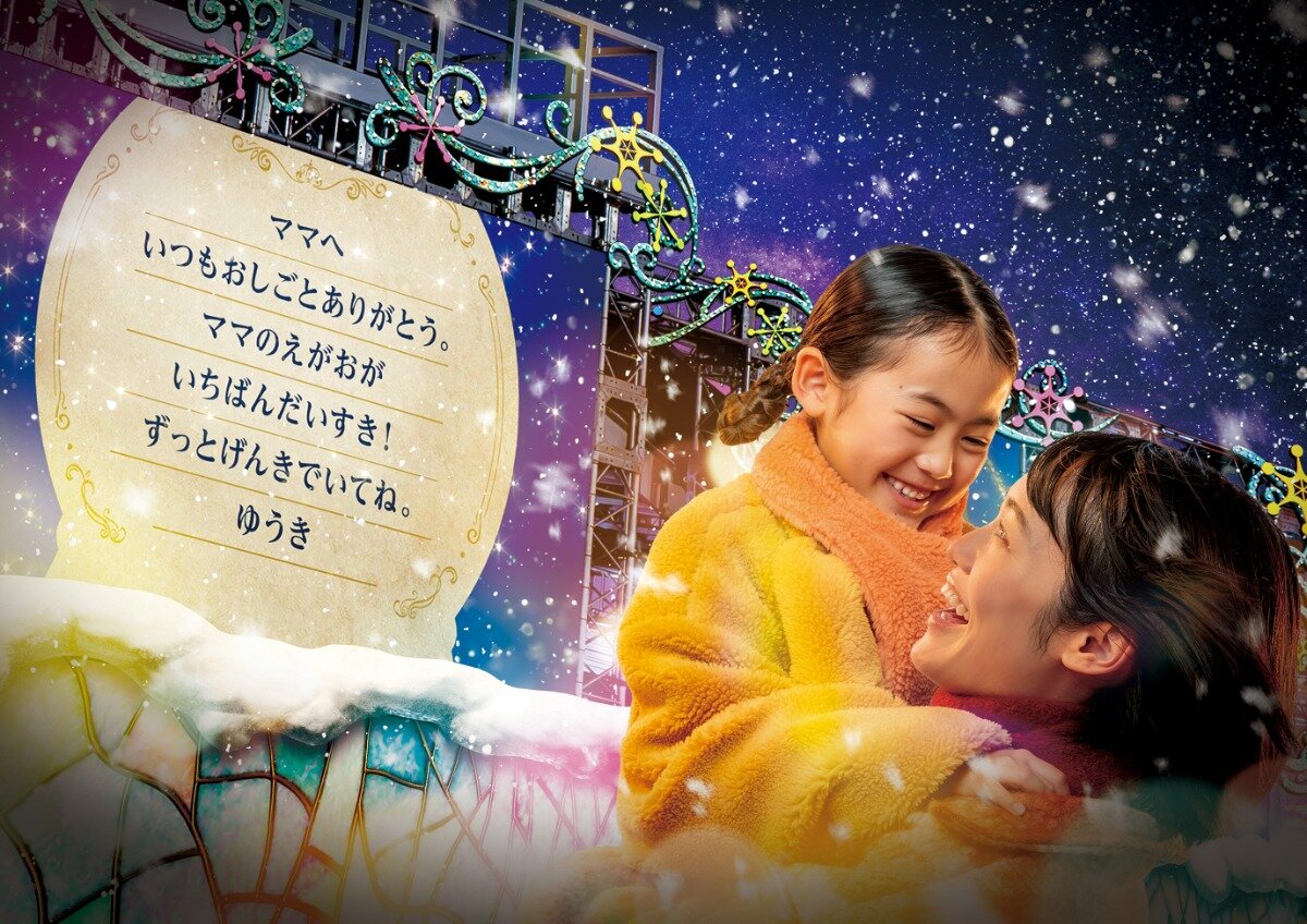 A parent and child beside a projected guest message during Joy of Lights