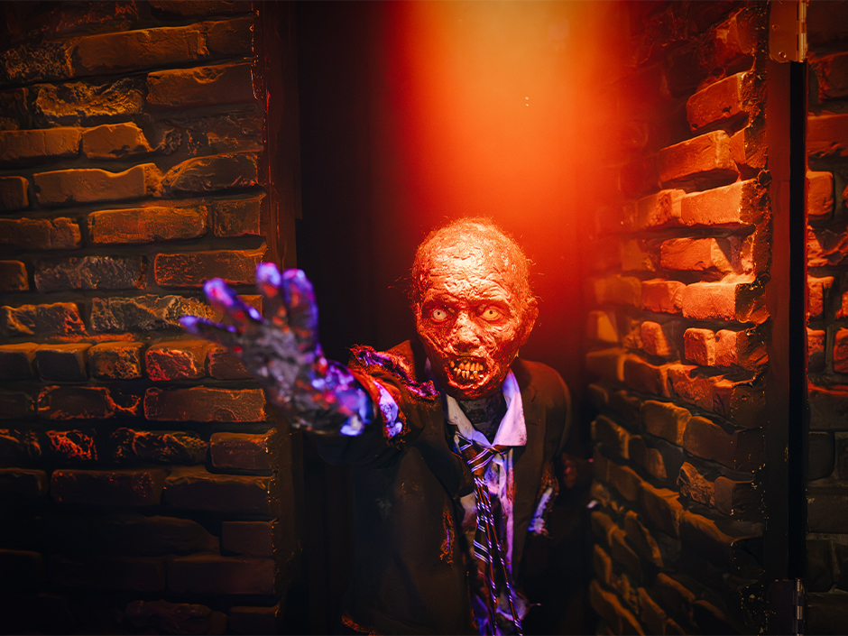 A decayed funeral-home character reaches toward guests inside Dead, Deader, Deadest