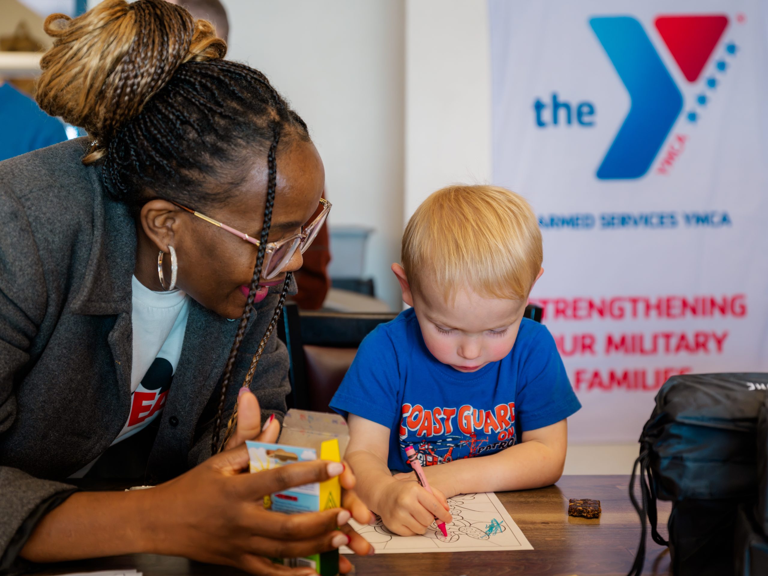 A child from a Coast Guard family colors beside an Armed Services YMCA representative in Juneau