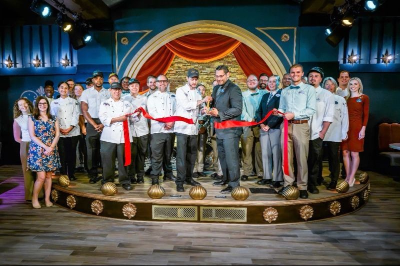 Cast Members gathered behind a red ribbon inside Hurly-Burly at Disney’s BoardWalk