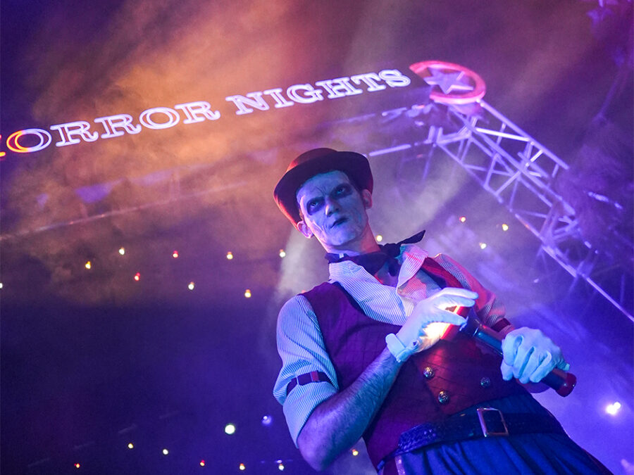 The Usher stands beneath the Halloween Horror Nights entrance in purple and orange fog