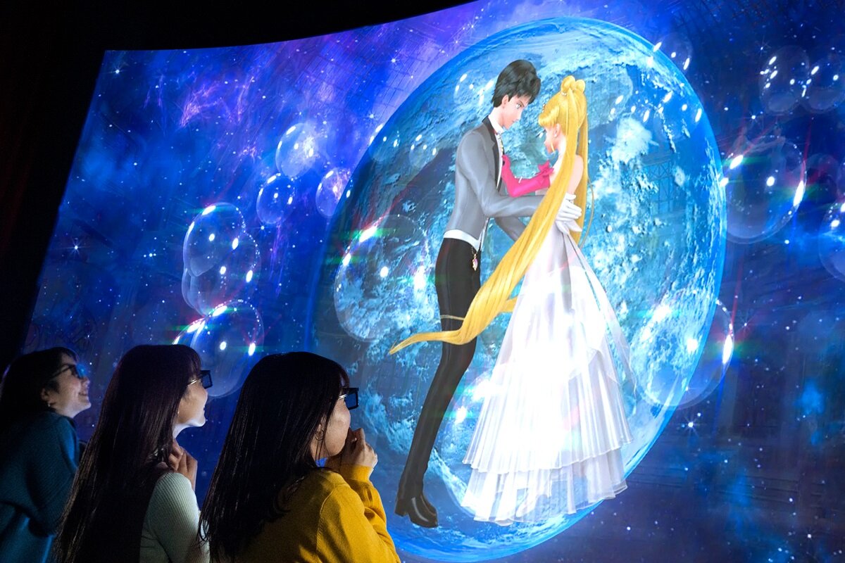 Guests watching Sailor Moon and Tuxedo Mask dance before a large moon inside the 4-D theater