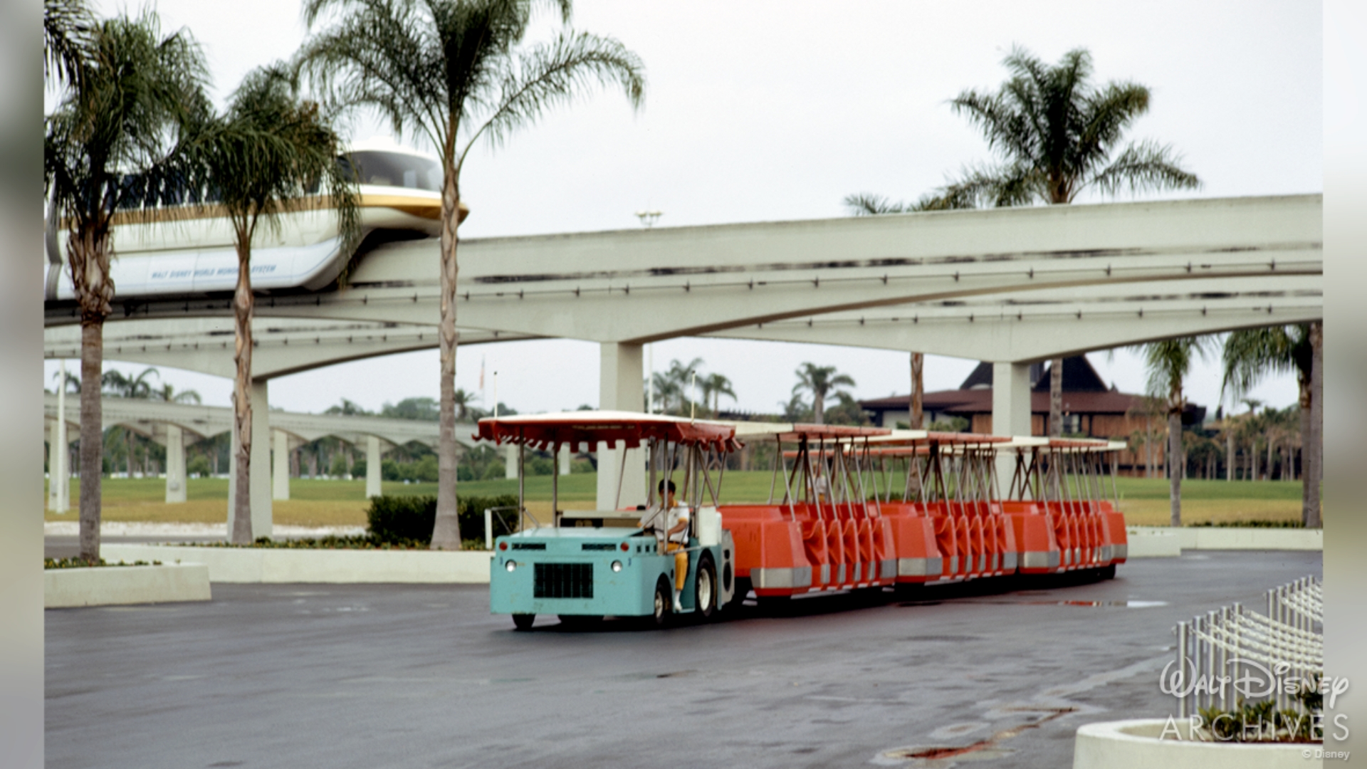 A gold-striped Monorail passes a brightly colored parking tram in April 1972
