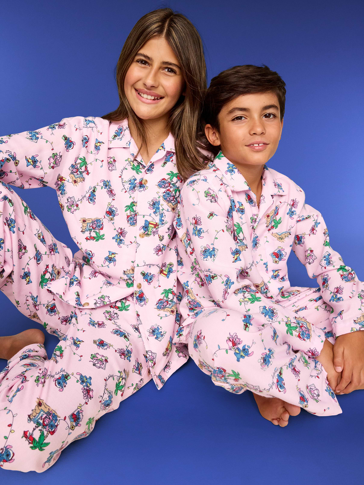Two children wearing pink Old Navy pajamas printed with Stitch and Angel holiday scenes