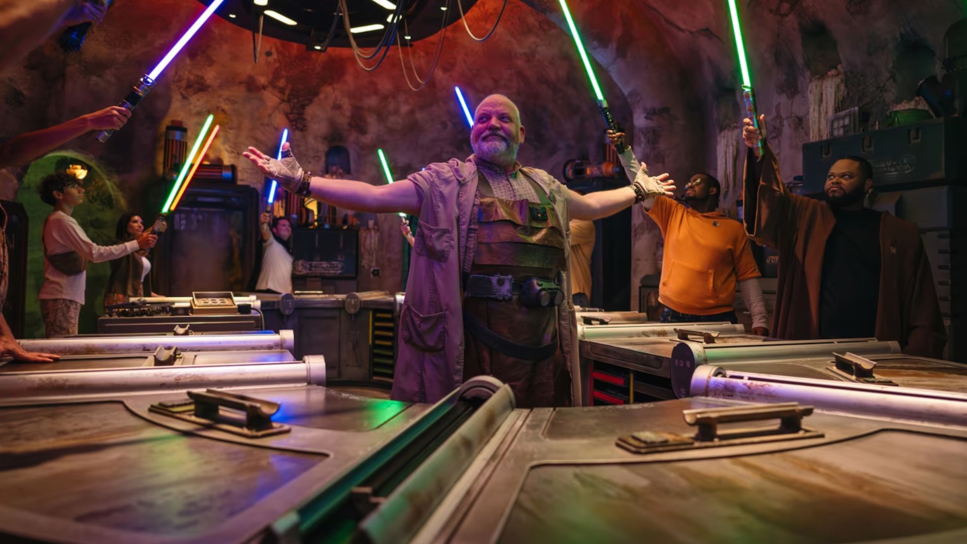A Savi’s Workshop Gatherer stands between builders holding illuminated lightsabers over component trays