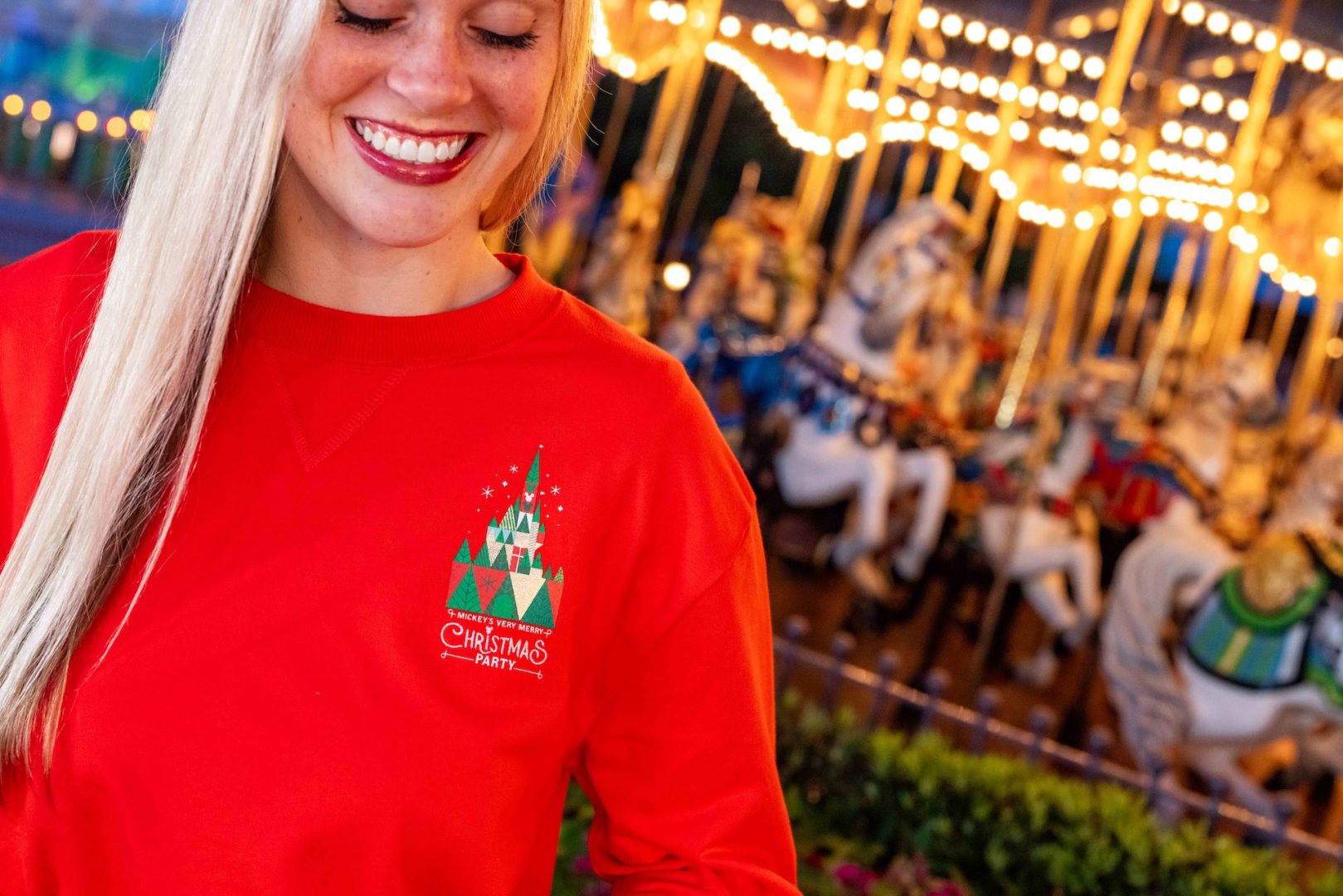 A red Mickey’s Very Merry Christmas Party pullover shown beside the Prince Charming Regal Carrousel at Magic Kingdom
