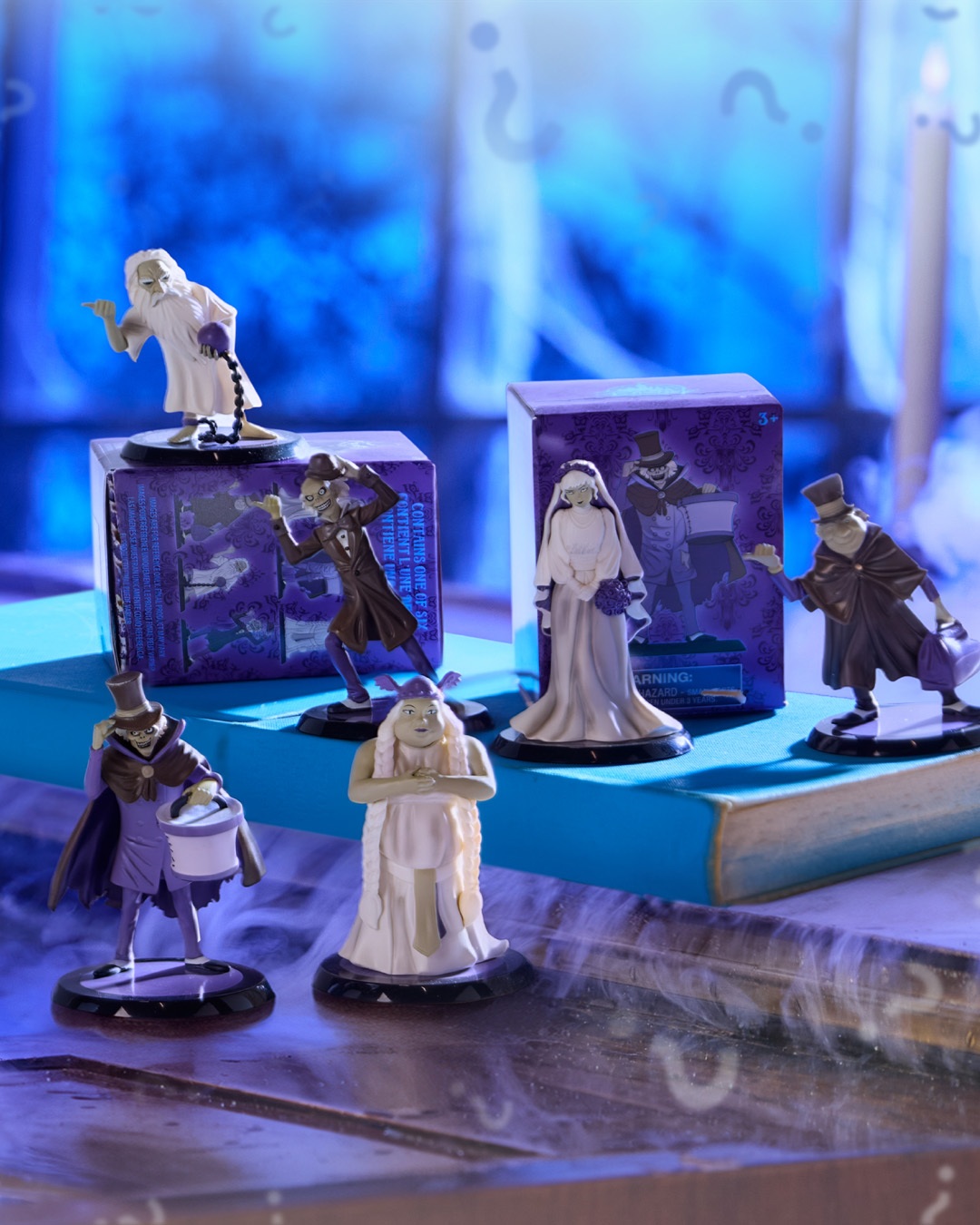 Six miniature Haunted Mansion figures arranged around two purple blind boxes in Disney Store’s official photo