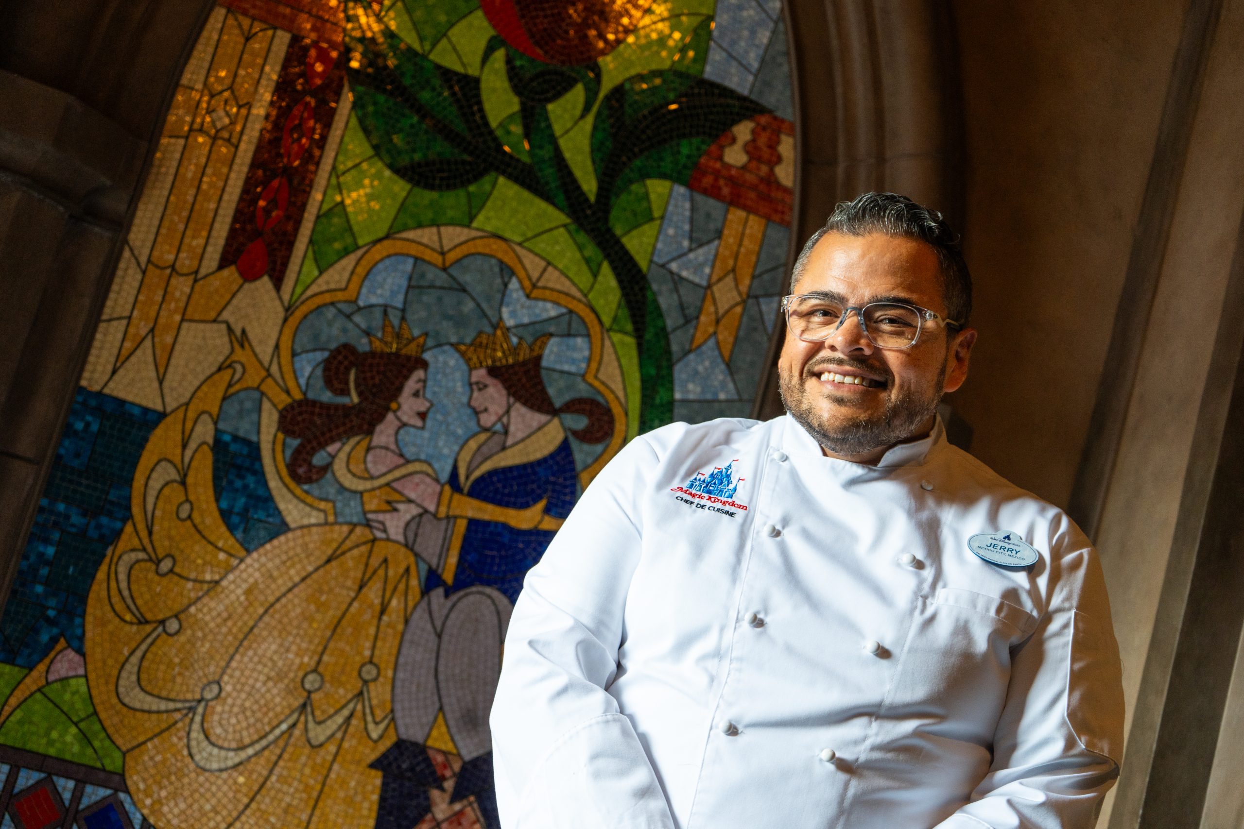 Gerardo “Jerry” Quijada Gonzalez in his chef’s coat beside a Beauty and the Beast mosaic at Be Our Guest Restaurant