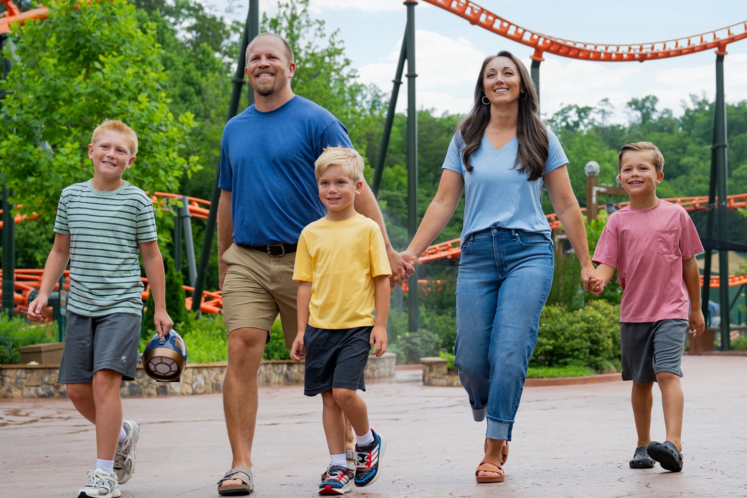 A family walks through Dollywood with an orange roller coaster track behind them