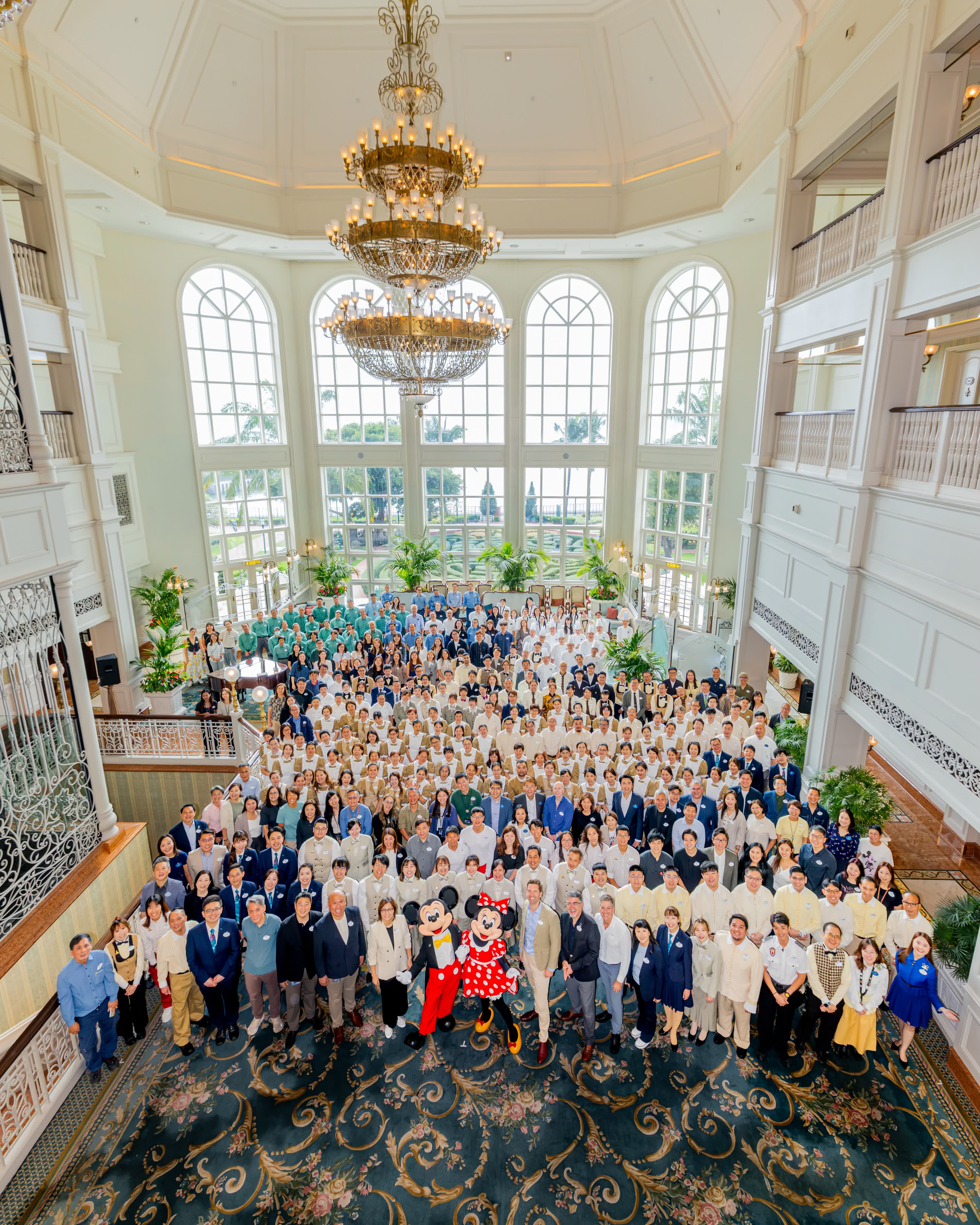 Hong Kong Disneyland Hotel Cast Members gather in the lobby beneath its chandeliers with Mickey and Minnie