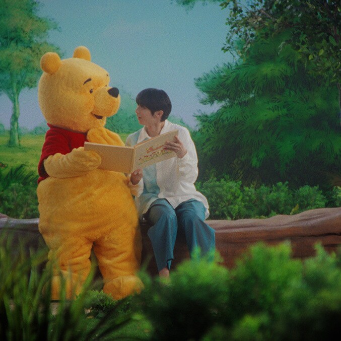 Yuzuru Hanyu sits beside Winnie the Pooh as they look through an album in Disney Japan’s centenary film