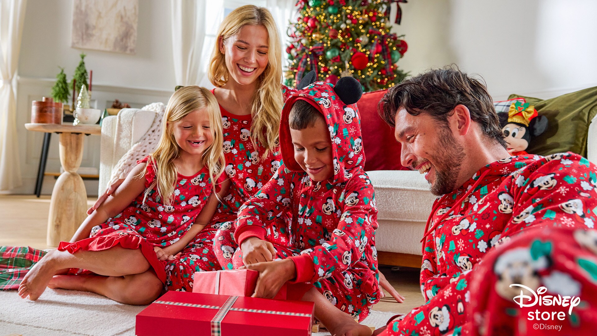 Family opening gifts in matching red Mickey holiday pajamas by a Christmas tree