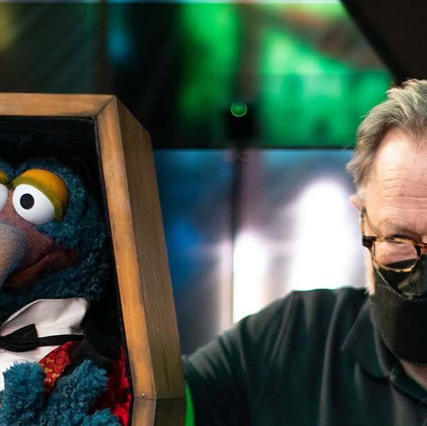 Gonzo poses in a coffin-shaped frame beside a masked Muppets Haunted Mansion performer