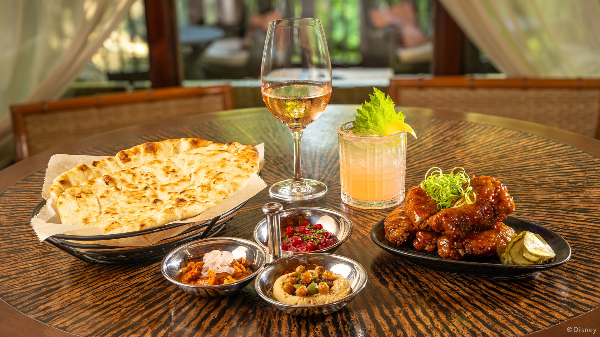 Nomad Lounge table with naan, three dips, chicken wings, wine and a cocktail