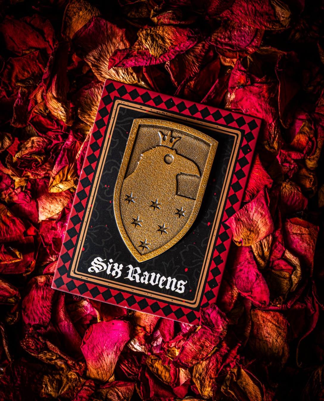 A collectible Six Ravens shield pin displayed on a black and red card over red and orange leaves