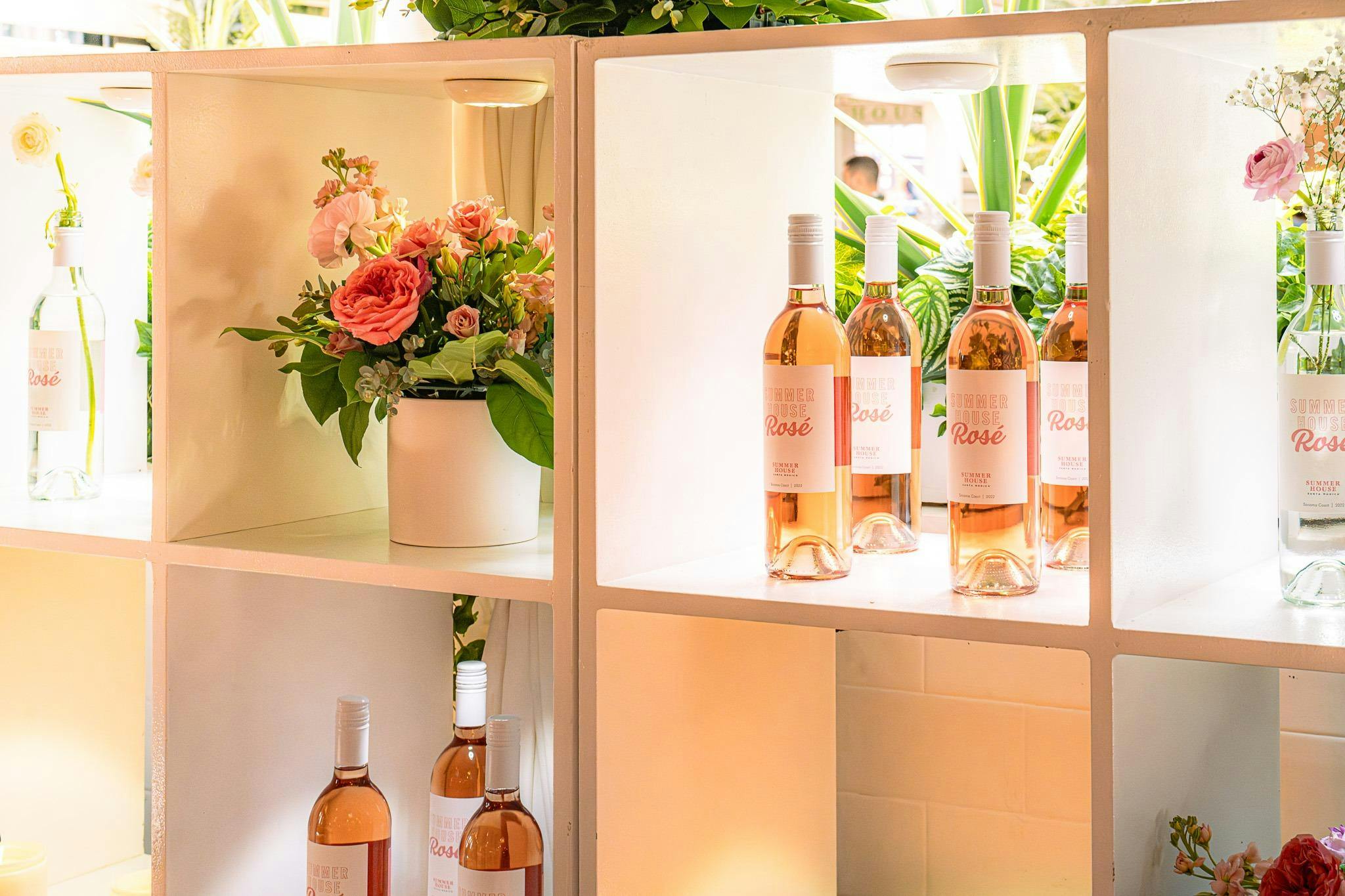 Summer House Rosé bottles and pink floral arrangements displayed in illuminated shelves