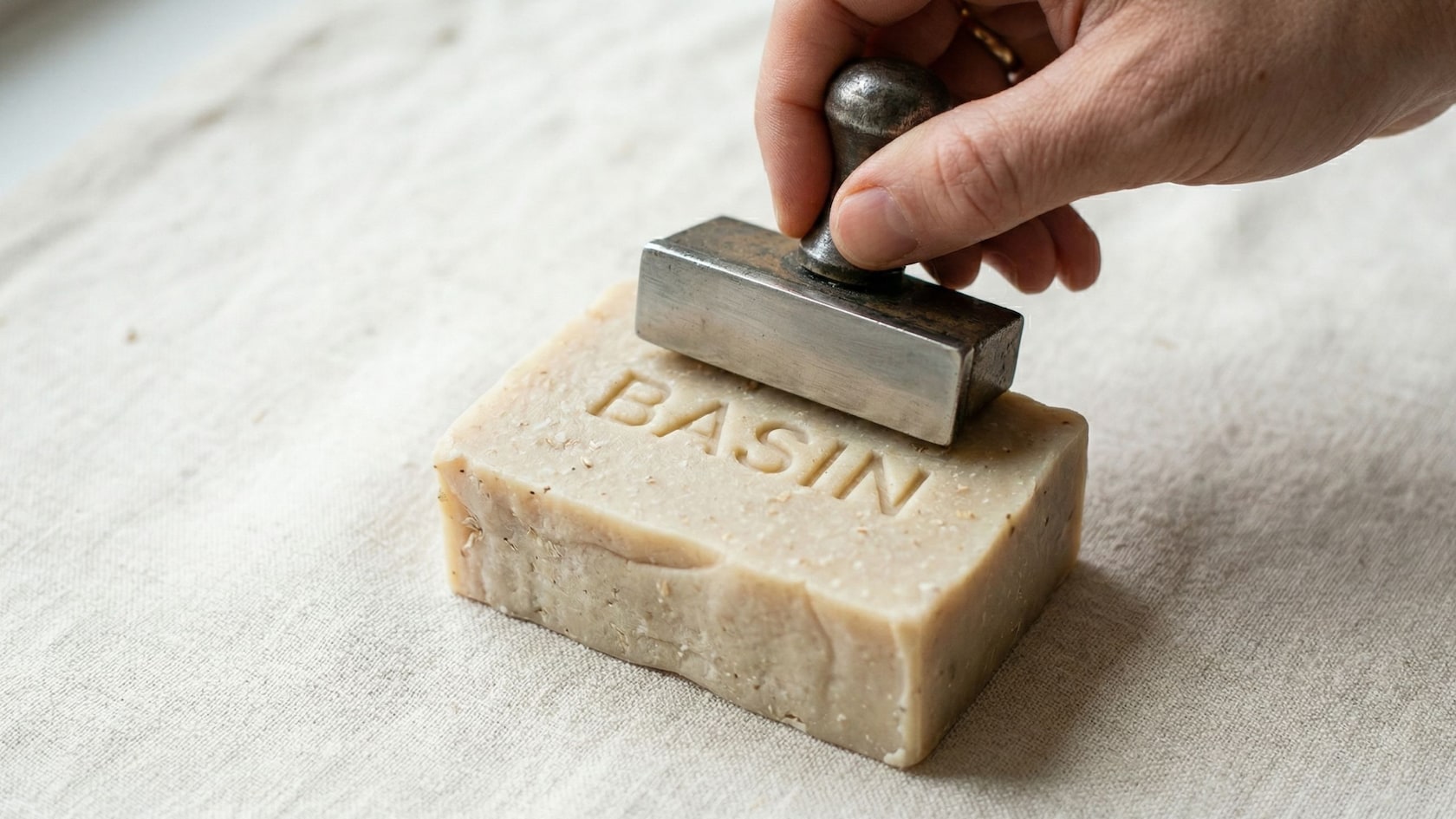 A hand embosses the Basin name into a bar of soap