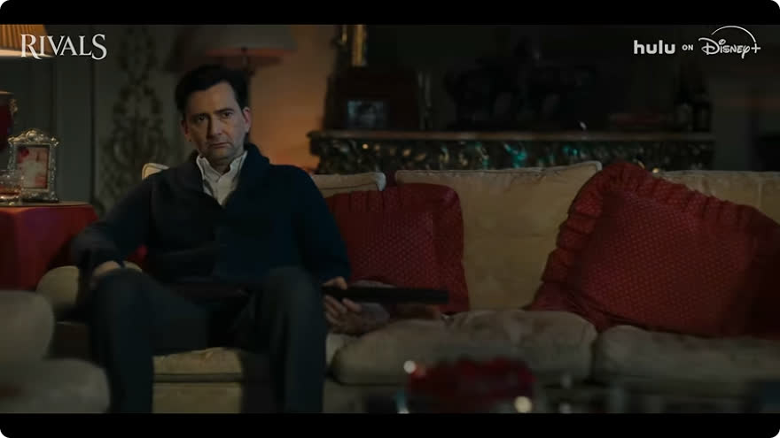 A man sits on a sofa in the Rivals Season 2 trailer