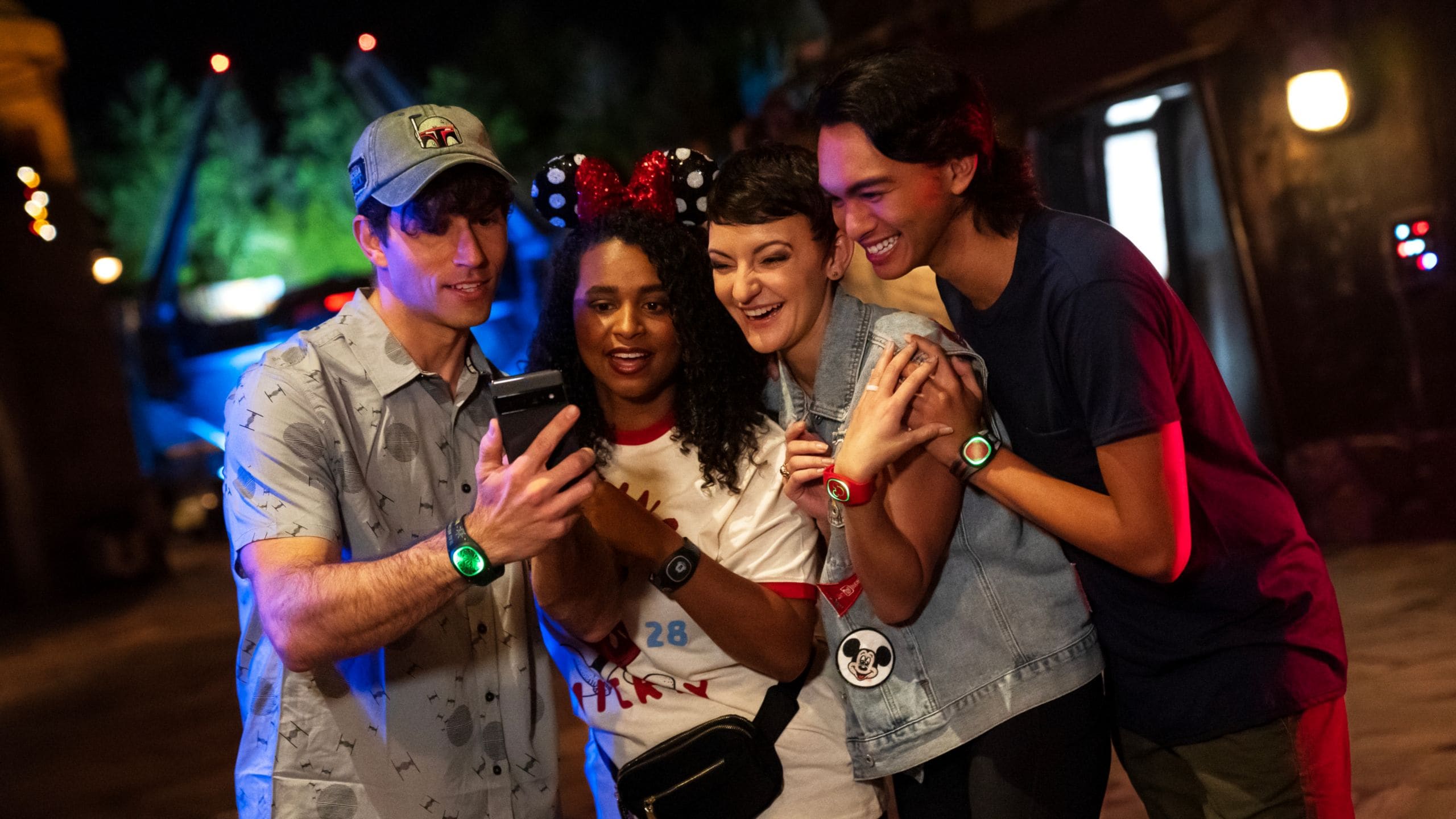 Four Walt Disney World guests use a phone while wearing MagicBands
