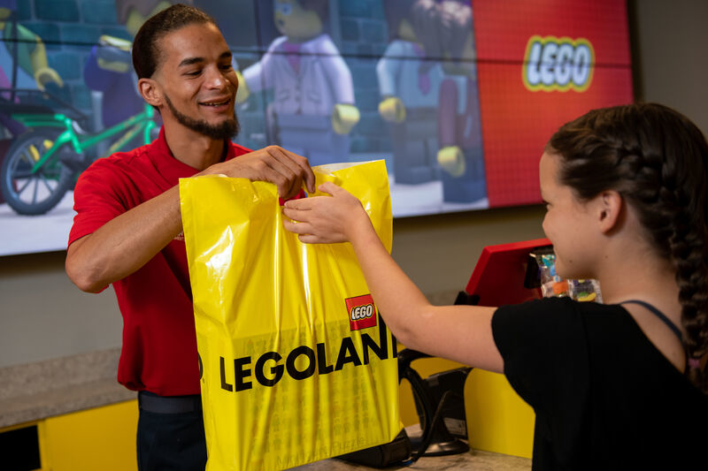 A LEGOLAND Florida retail worker hands a guest a yellow LEGOLAND shopping bag