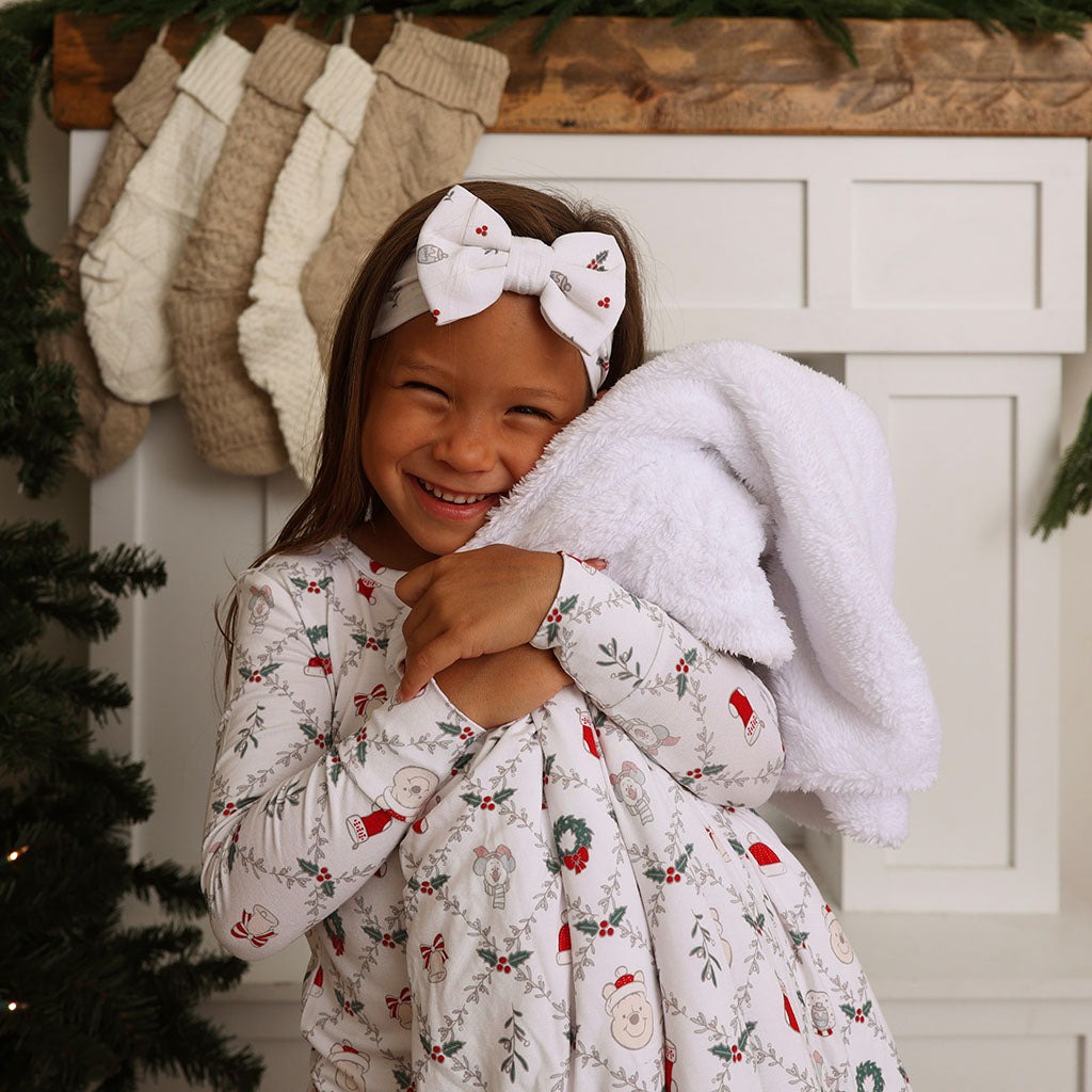 Child wearing Holiday Pooh pajamas while holding a white plush blanket