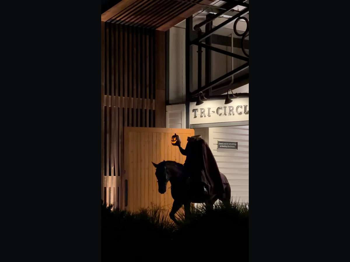 The Headless Horseman holds a glowing jack-o’-lantern beside a horse outside Tri-Circle-D Ranch