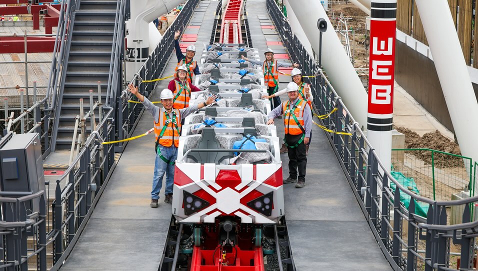 Shanghai Disney Imagineers stand beside a Spider-Man coaster train on its red track