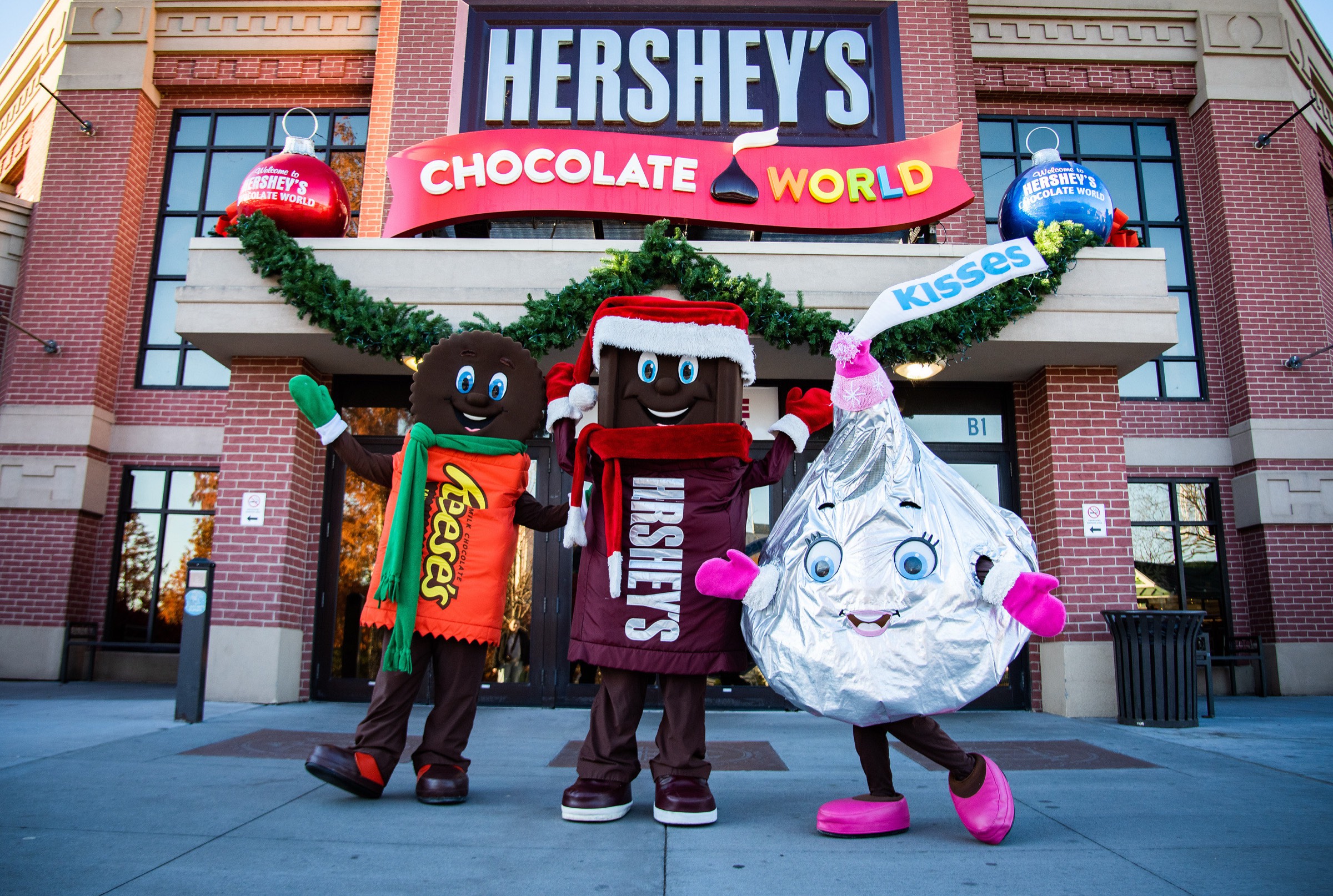 Reese, Hersh and Kiss characters in holiday outfits outside Hershey’s Chocolate World