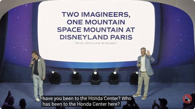 Imagineers Michel Den Dulk and Tim Delaney onstage at D23 Center Stage beneath a Space Mountain at Disneyland Paris title screen