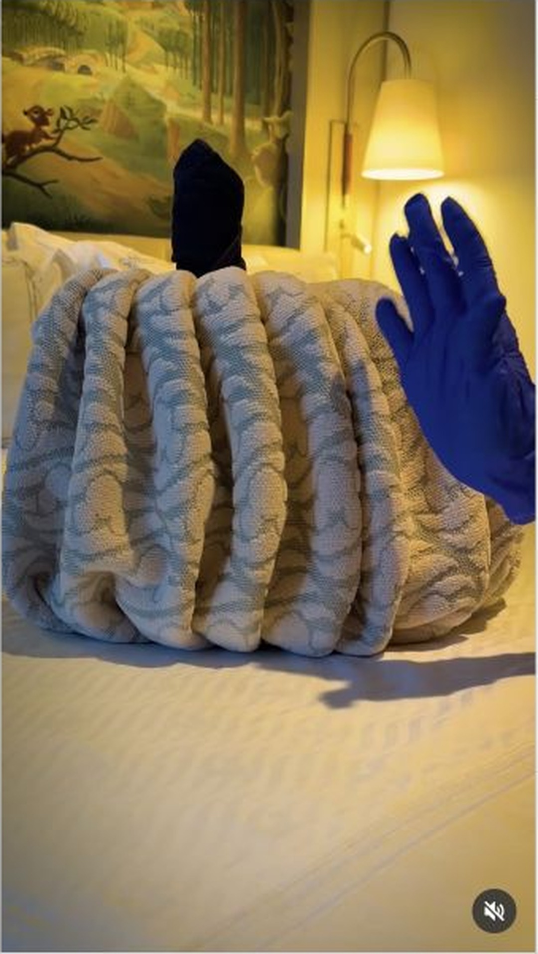 A gray ribbed towel folded into a pumpkin with a dark stem on a Disney Cruise Line stateroom bed