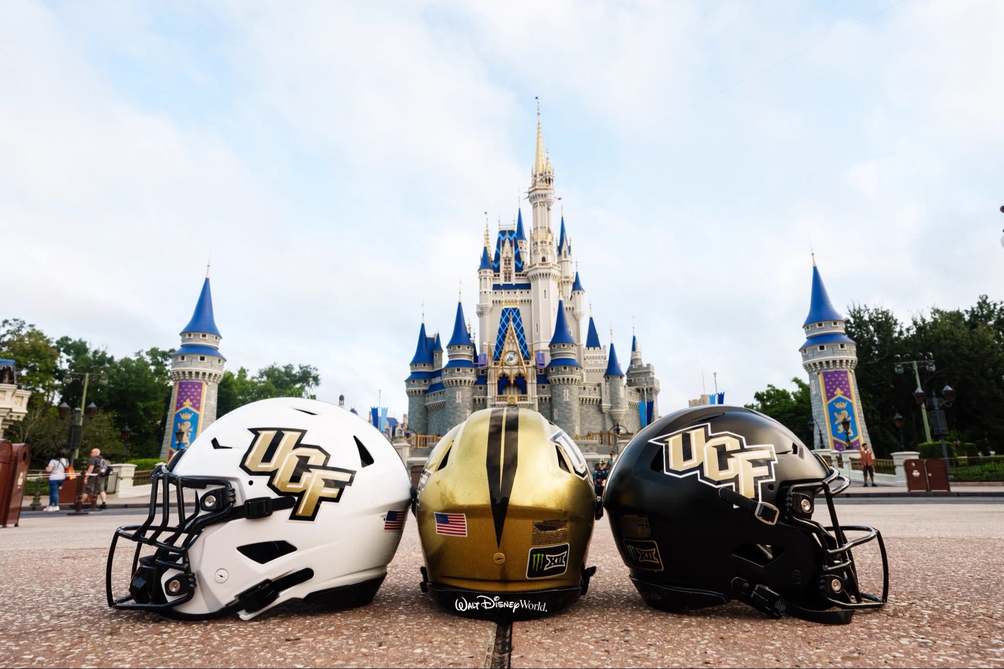 Two UCF football helmets and a gold Walt Disney World helmet in front of Cinderella Castle