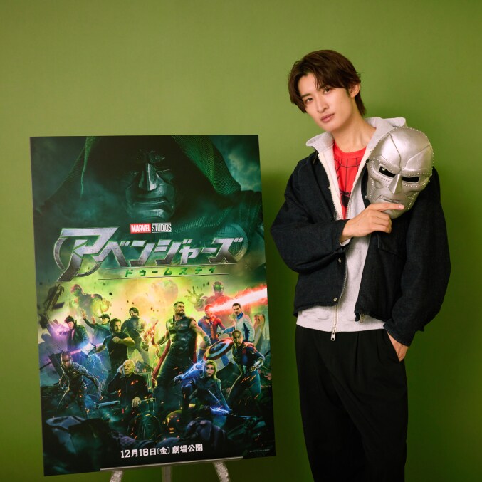 Koji Mukai holds a Doctor Doom mask beside Avengers: Doomsday artwork