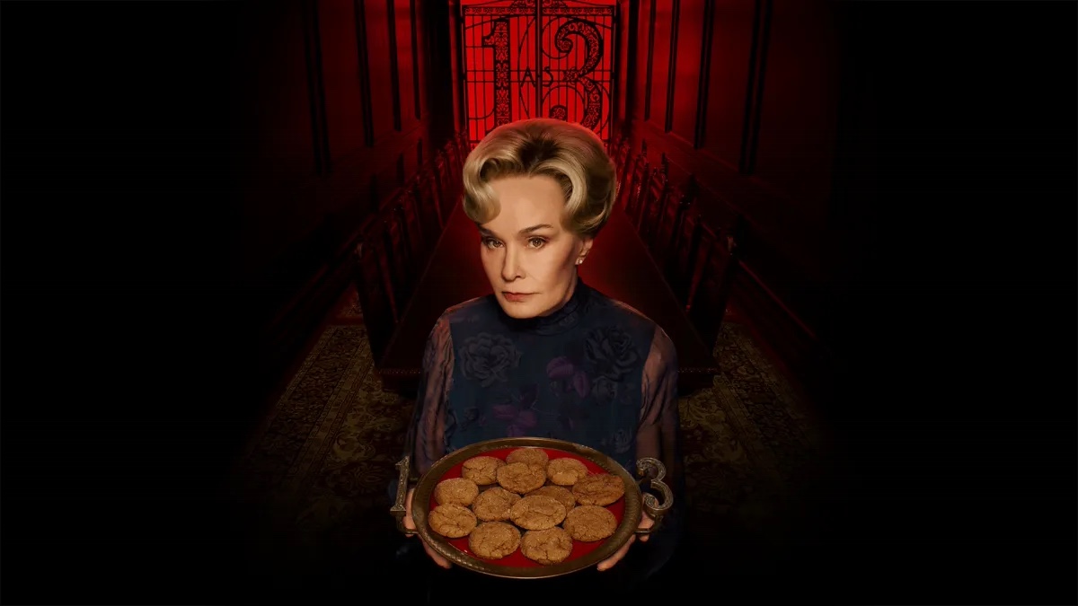 Jessica Lange stands in a red-lit corridor holding a tray of cookies in American Horror Story: 13 promotional art