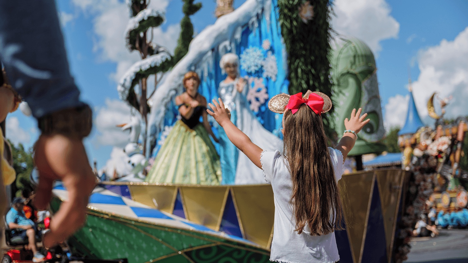 A child reaches toward Anna and Elsa during a Magic Kingdom parade