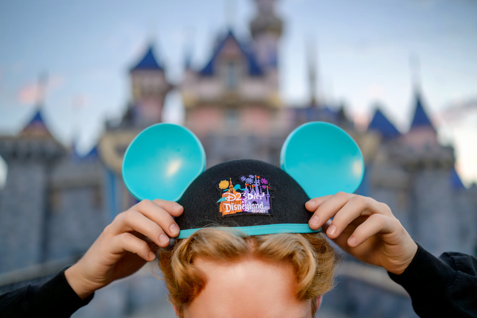 Blue D23 Day Mickey ear hat in front of Sleeping Beauty Castle