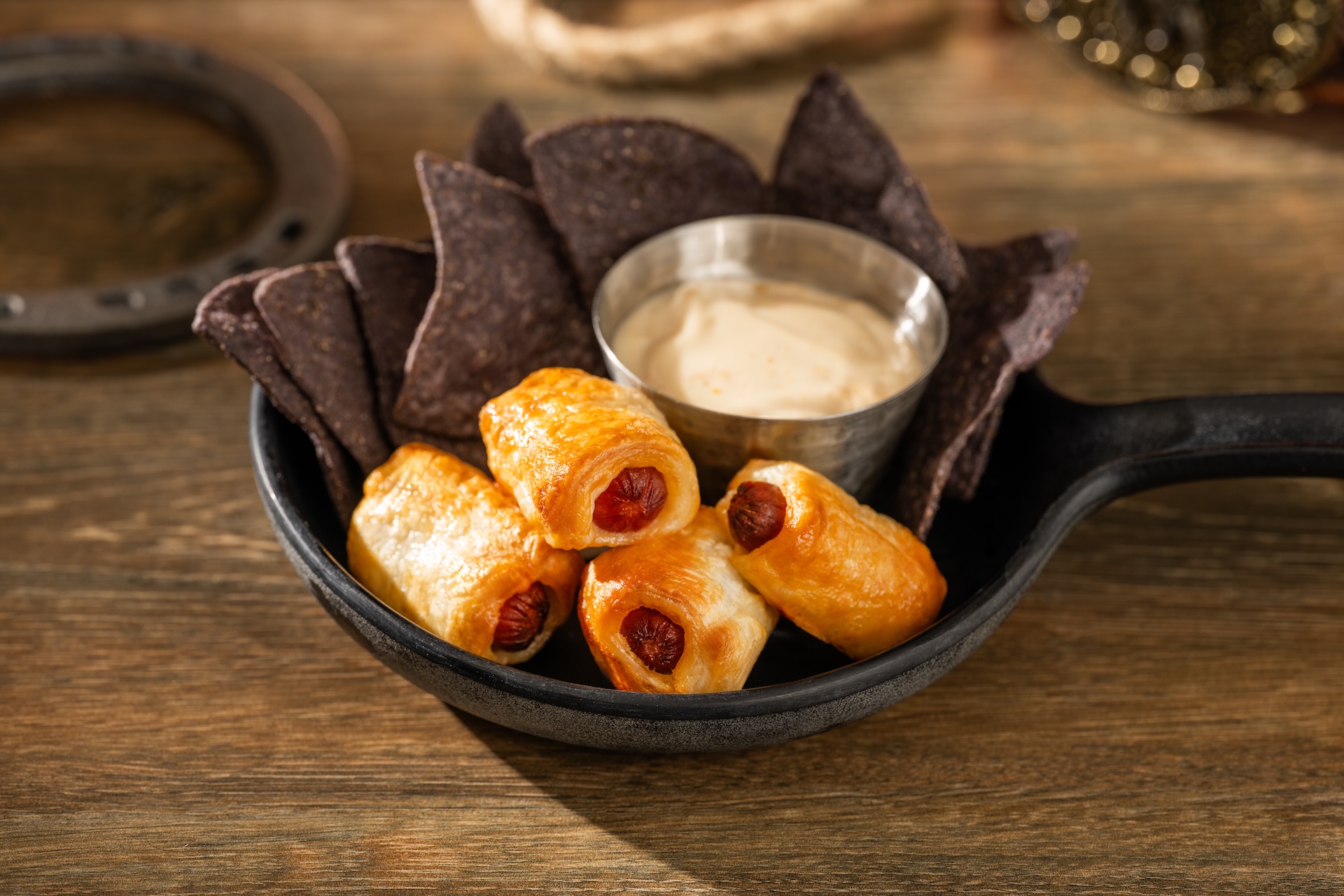 Mini hot dogs wrapped in pastry with tortilla chips and queso