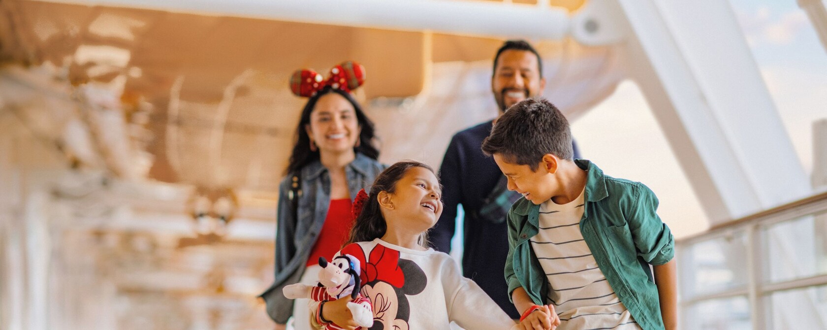 A smiling family walks together on the deck of a Disney Cruise Line ship