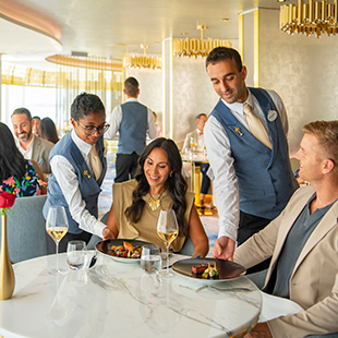 Two Disney Cruise Line dining servers placing dishes for guests at a restaurant table