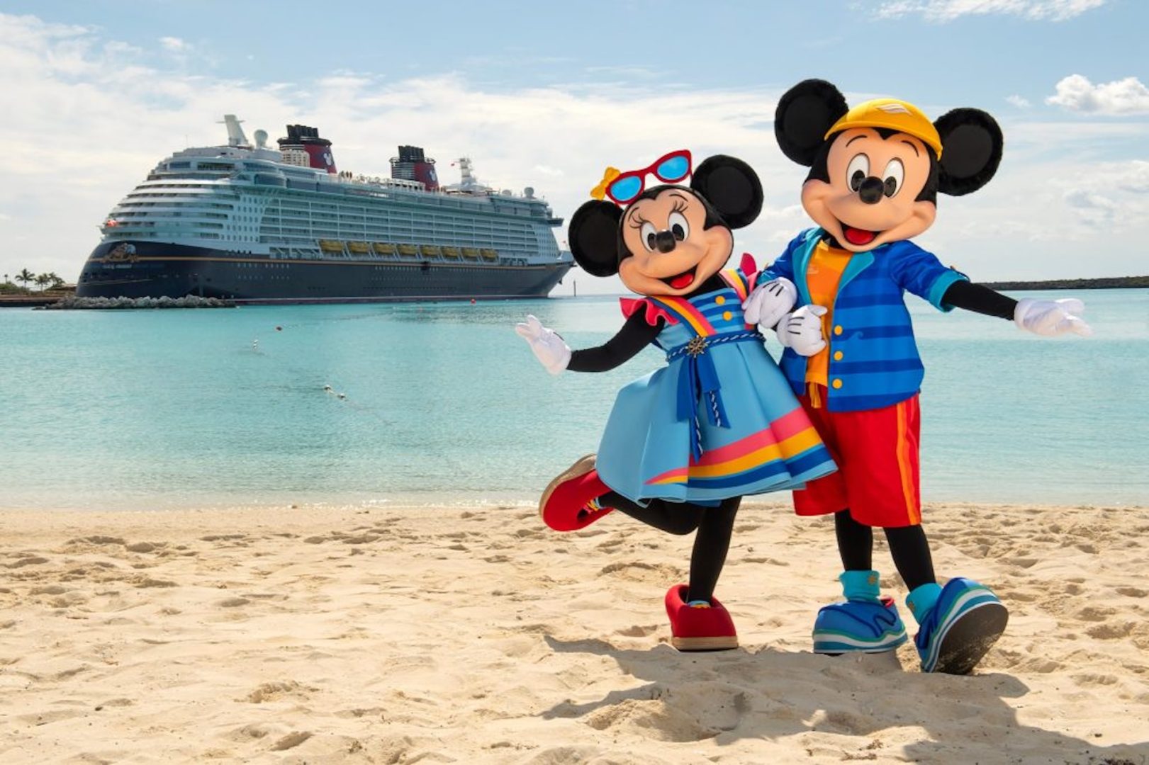Mickey and Minnie standing on a beach with a Disney Cruise Line ship in the distance