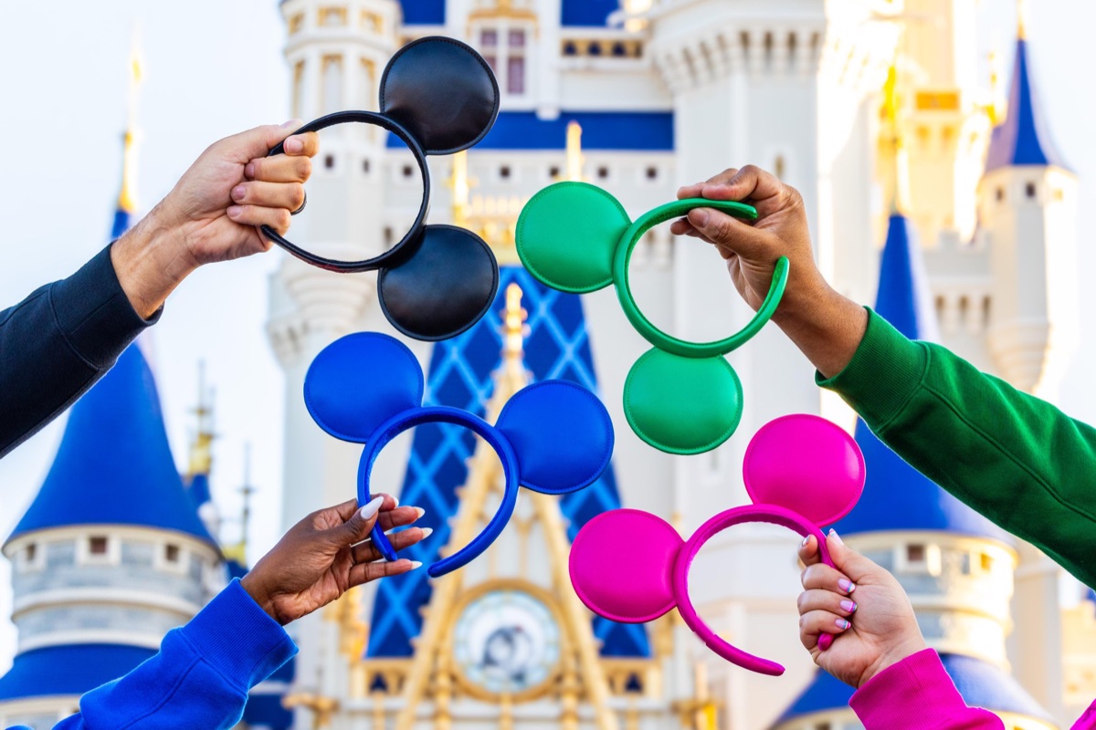 Black, blue, green, and pink Mickey ear headbands from the Disney Parks Logo Mania Collection in front of Cinderella Castle