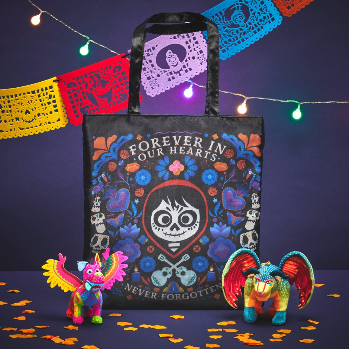 A Coco tote bag displayed with colorful alebrije figures, papel picado and string lights