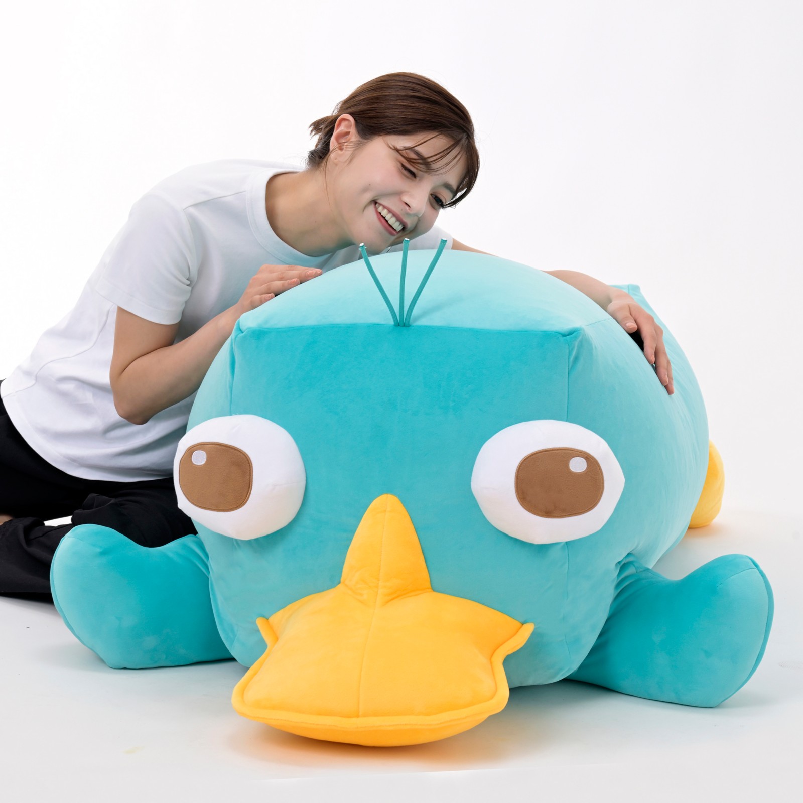 A person leaning over a 138-centimeter Perry the Platypus plush