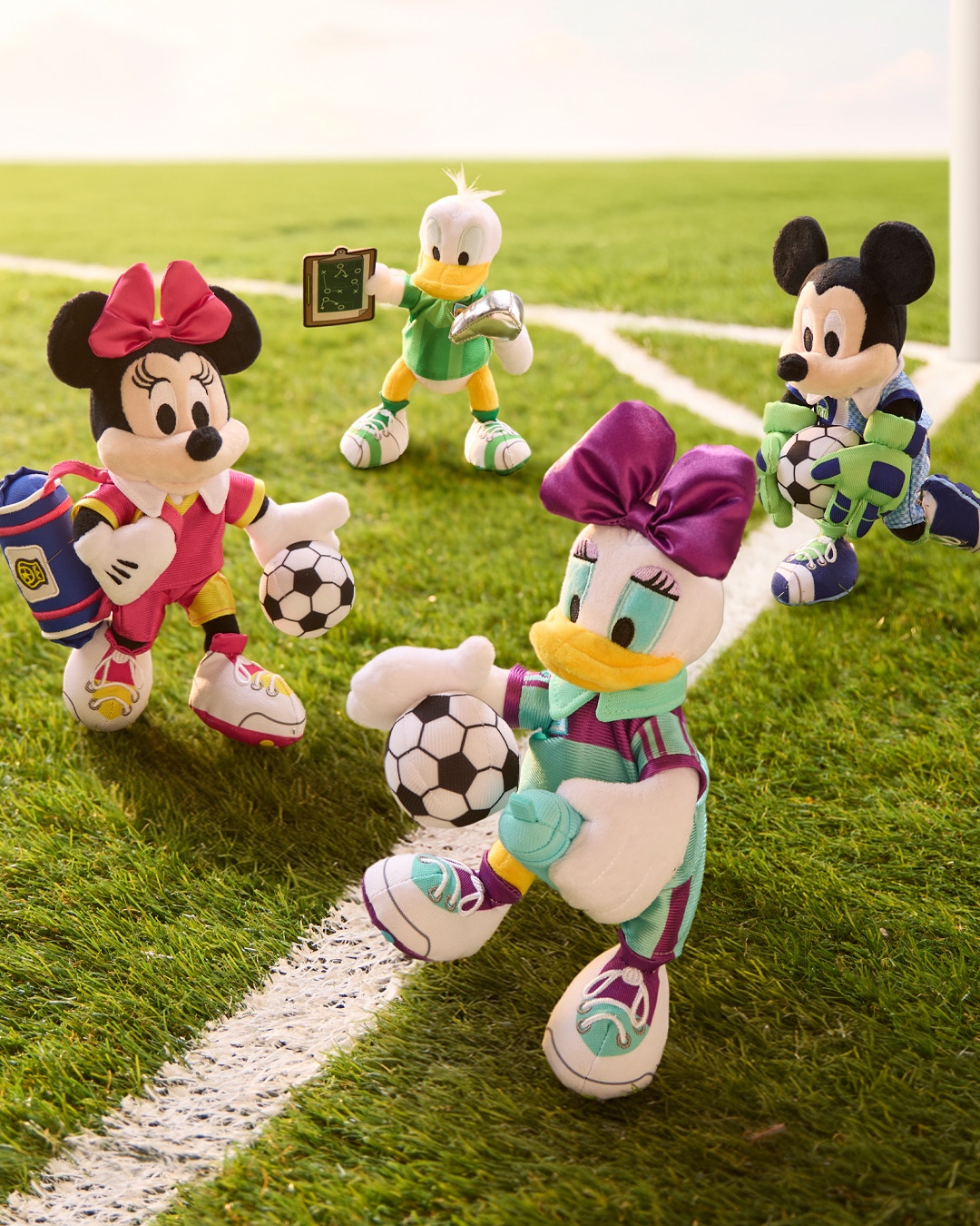 Minnie, Daisy, Donald, and Mickey soccer plushes on a soccer field
