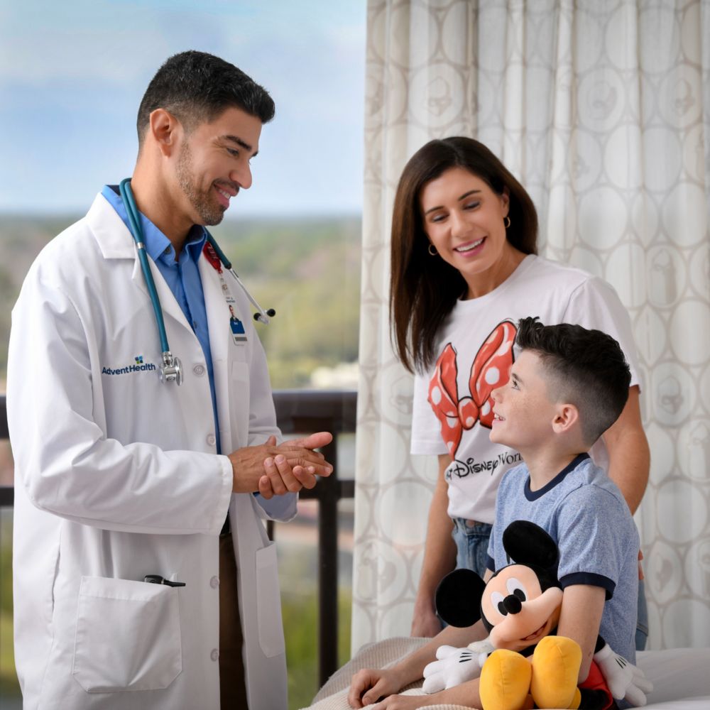 An AdventHealth physician speaks with a mother and child during a Disney World Resort hotel room visit