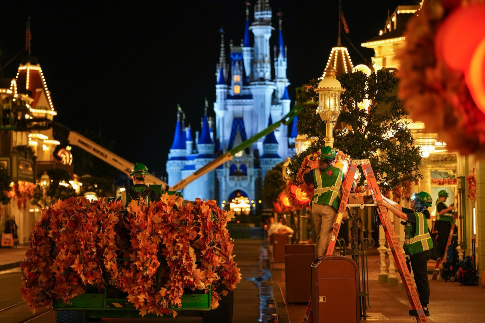 Cast members install fall decorations on Main Street U.S.A. with Cinderella Castle behind them