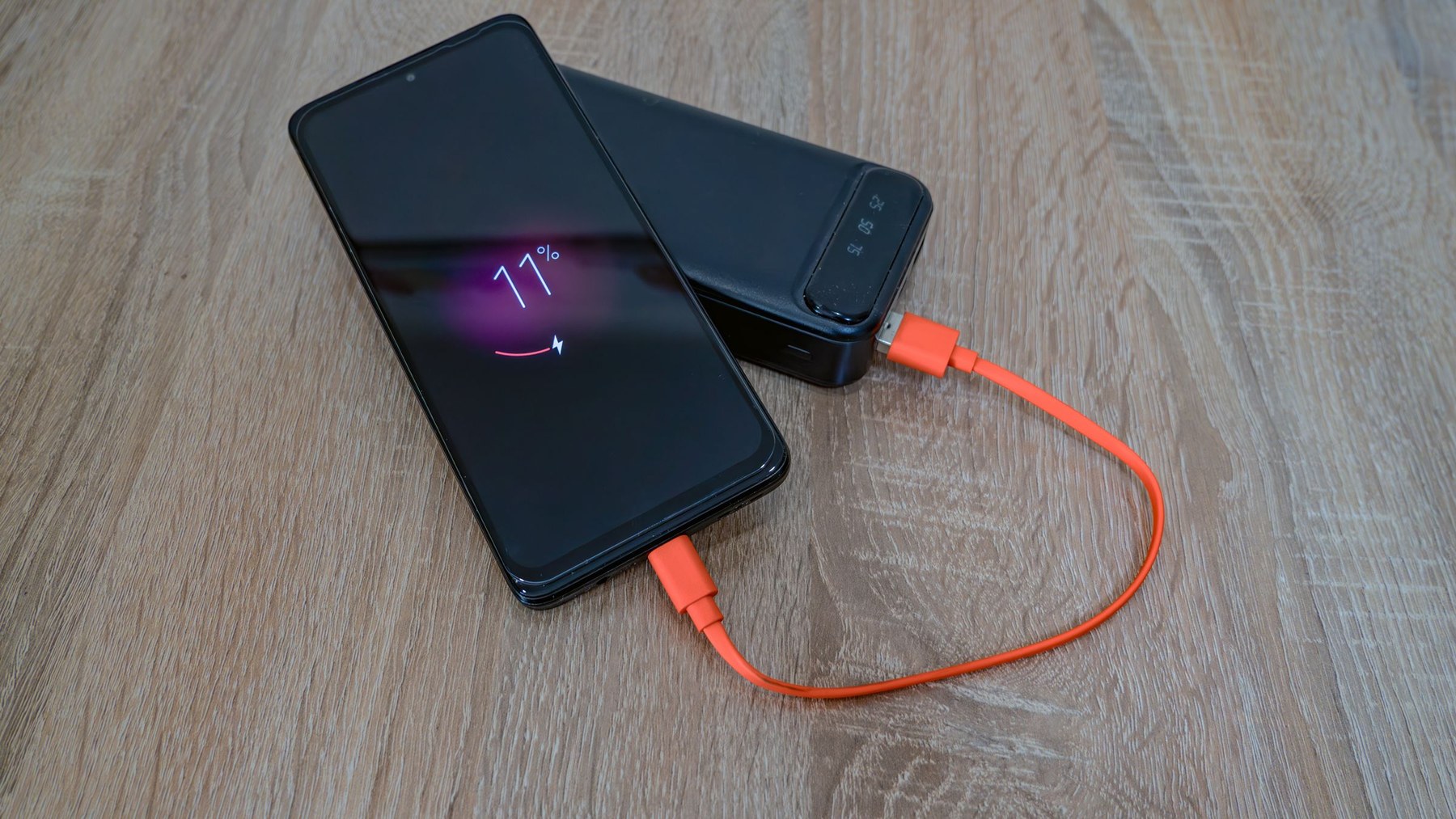 A smartphone connected to a portable power bank with an orange charging cable