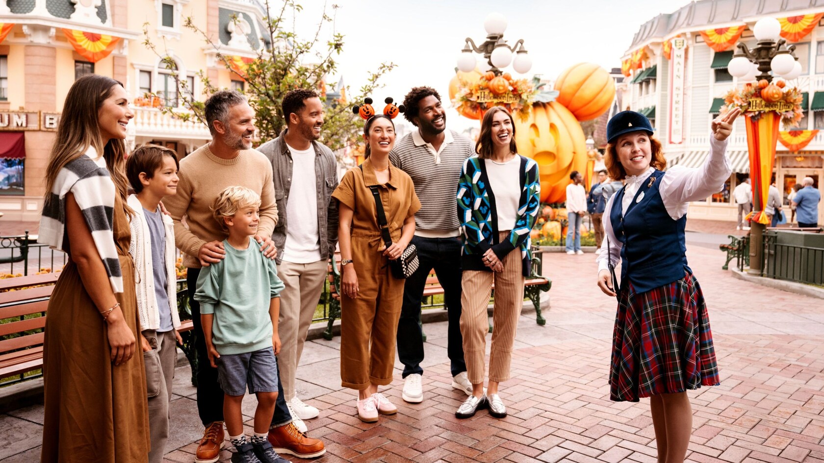 A Disneyland tour guide holding a lantern with Halloween-costumed guests on Main Street, U.S.A.